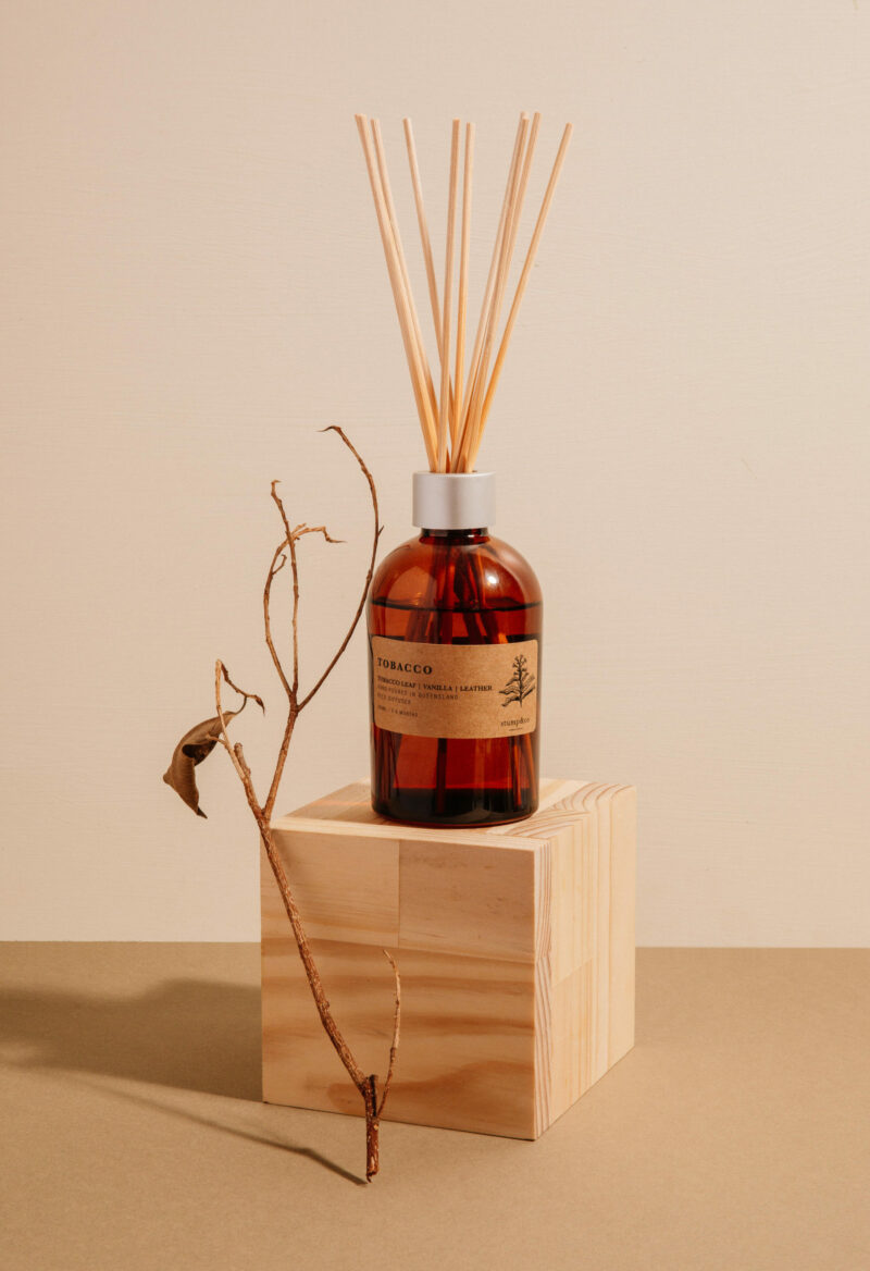 Stump Co Diffuser resting on wooden box and styled with tobacco leaf branch